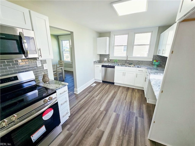 kitchen featuring light stone counters, stainless steel appliances, dark wood-type flooring, a sink, and white cabinetry