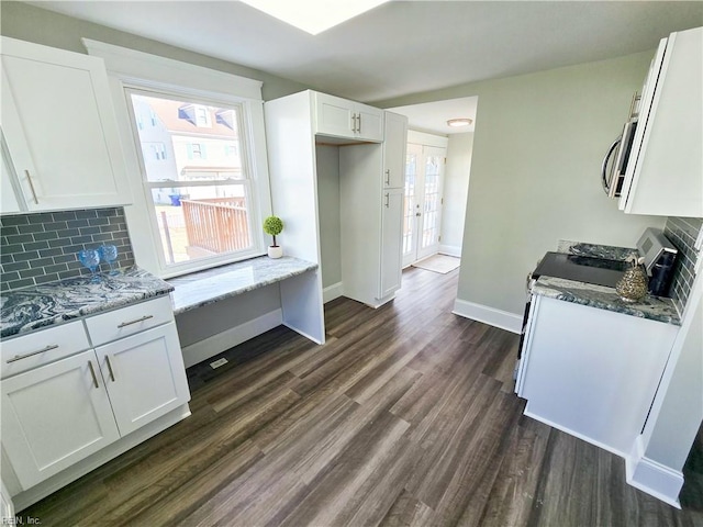 kitchen with stainless steel microwave, decorative backsplash, dark wood-type flooring, white cabinets, and baseboards