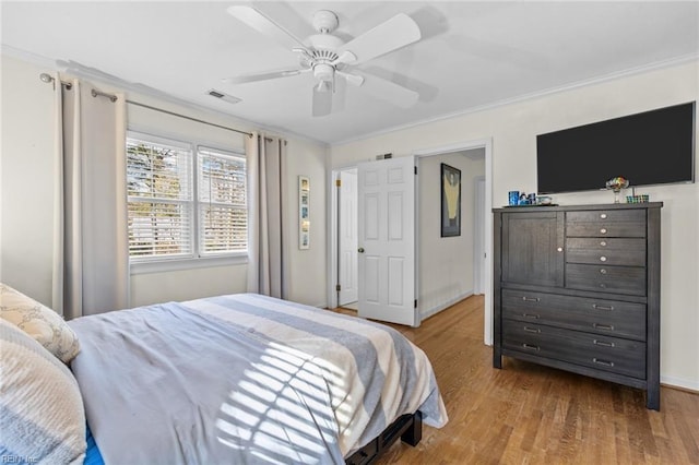 bedroom with ceiling fan, wood finished floors, visible vents, baseboards, and ornamental molding