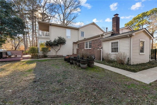 rear view of property featuring a deck, a balcony, brick siding, a yard, and a chimney