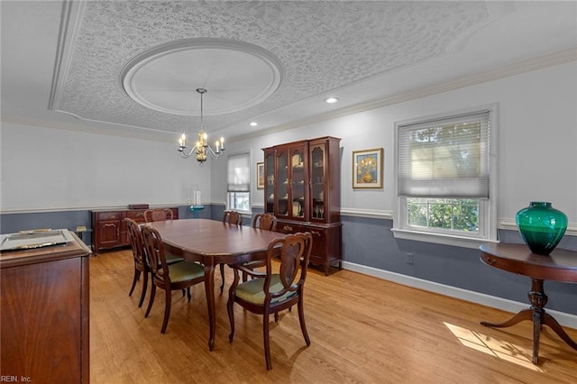 dining room featuring crown molding, a textured ceiling, a raised ceiling, and light wood-style floors