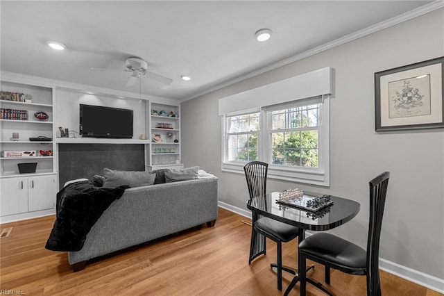 living room featuring light wood finished floors, baseboards, a ceiling fan, crown molding, and built in shelves