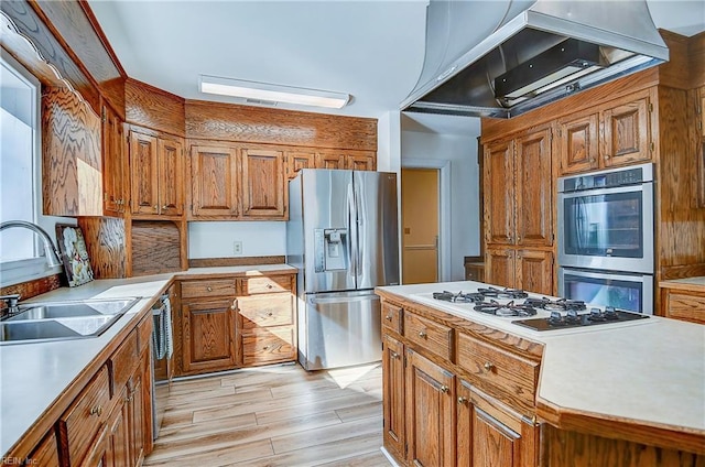 kitchen with brown cabinetry, wall chimney exhaust hood, stainless steel appliances, light countertops, and a sink