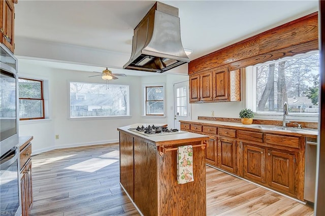 kitchen with a center island, island exhaust hood, appliances with stainless steel finishes, brown cabinetry, and a sink