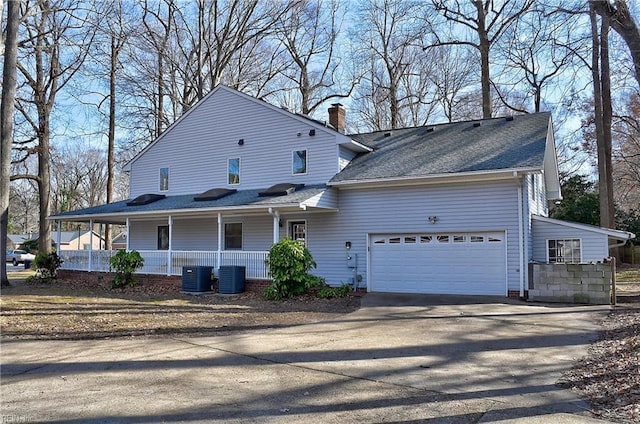 exterior space with a porch, an attached garage, central air condition unit, concrete driveway, and a chimney