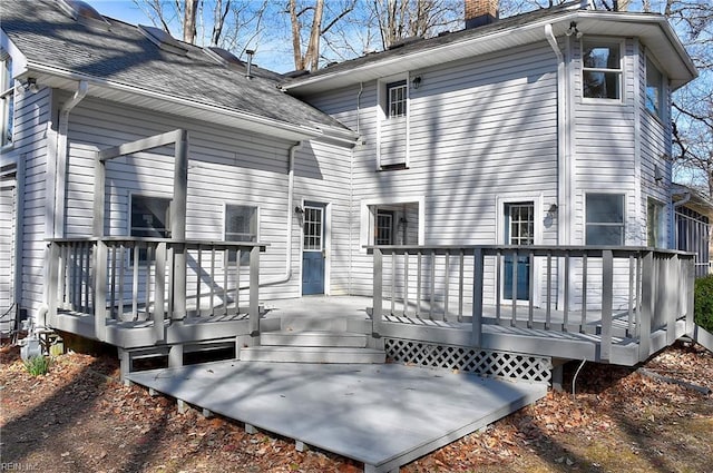 back of house with a shingled roof, a chimney, and a wooden deck