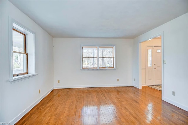 empty room with plenty of natural light, baseboards, and light wood-style flooring