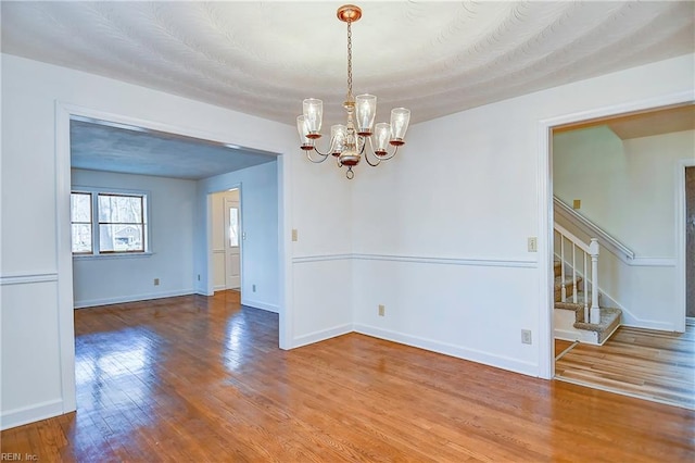 unfurnished room with stairs, an inviting chandelier, wood finished floors, and baseboards