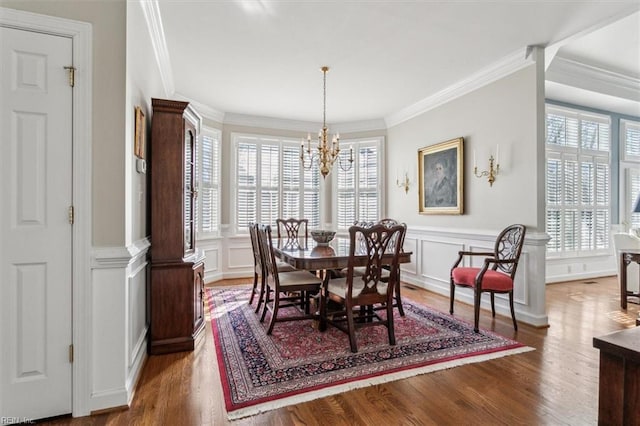 dining space with a wainscoted wall, crown molding, a decorative wall, an inviting chandelier, and wood finished floors