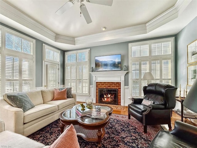 interior space with a ceiling fan, a tray ceiling, and a brick fireplace