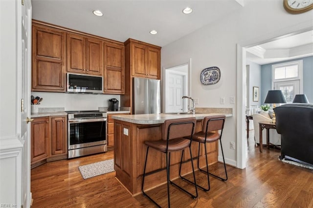 kitchen featuring dark wood-style flooring, appliances with stainless steel finishes, brown cabinetry, and a sink