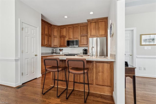 kitchen featuring stainless steel appliances, wood finished floors, a sink, light countertops, and brown cabinets