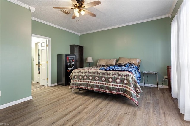 bedroom with crown molding, a textured ceiling, baseboards, and wood finished floors