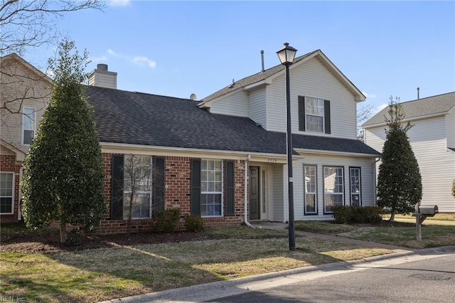 traditional-style home featuring a shingled roof, a front yard, brick siding, and a chimney