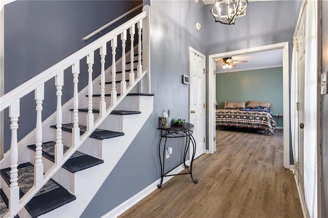 staircase with ornamental molding, ceiling fan with notable chandelier, baseboards, and wood finished floors