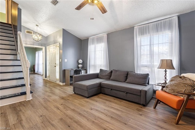 living room with lofted ceiling, visible vents, light wood-style floors, a textured ceiling, and stairs