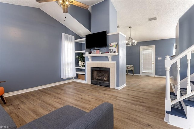 living area with lofted ceiling, a tile fireplace, wood finished floors, visible vents, and stairs