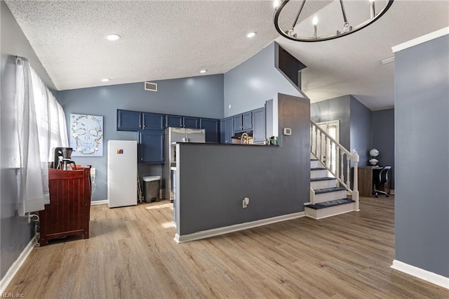 kitchen featuring lofted ceiling, blue cabinetry, light wood-style floors, and freestanding refrigerator