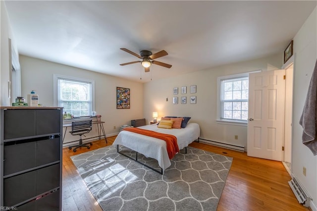 bedroom featuring multiple windows, baseboard heating, and wood finished floors