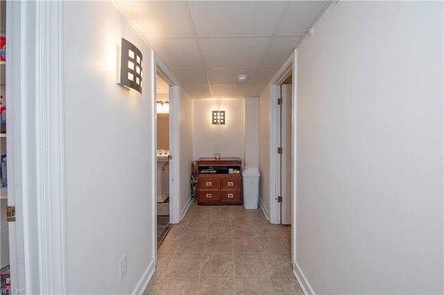 hallway featuring light tile patterned floors, baseboards, and a paneled ceiling