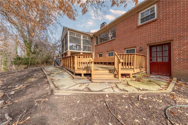 rear view of house with brick siding, a chimney, a wooden deck, and a sunroom