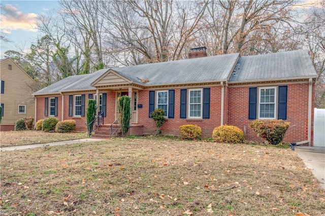 ranch-style home featuring brick siding, a chimney, and a front lawn