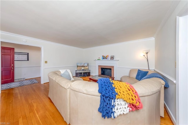 living area featuring crown molding, a brick fireplace, and light wood-type flooring