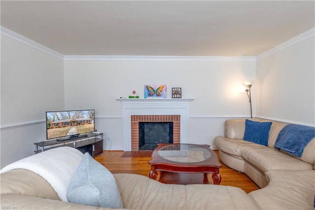 living room with a brick fireplace, wood finished floors, and crown molding