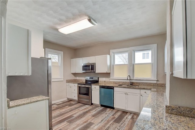 kitchen with white cabinets, light stone countertops, stainless steel appliances, and a sink