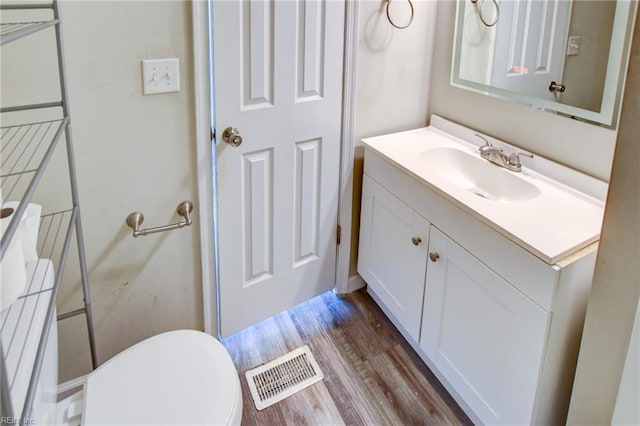 half bath with visible vents, vanity, toilet, and wood finished floors