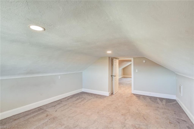 bonus room with a textured ceiling, vaulted ceiling, light colored carpet, and baseboards