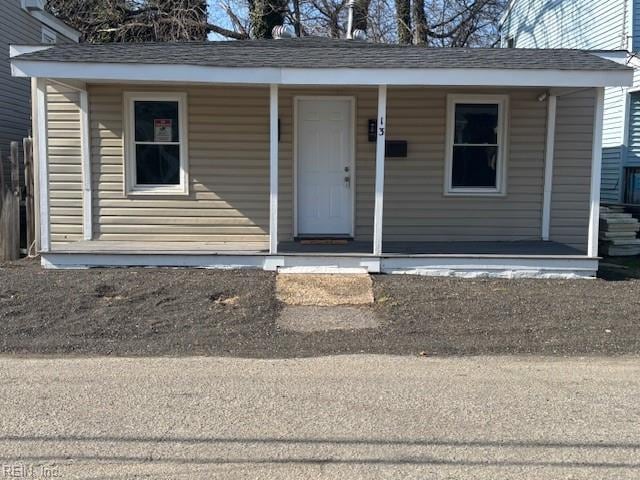 view of exterior entry with a porch and roof with shingles