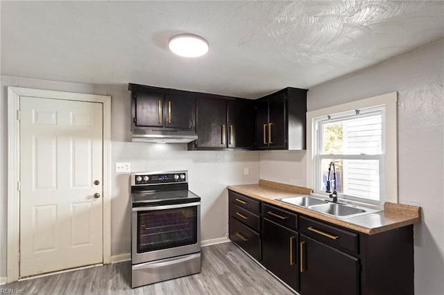 kitchen with electric stove, light wood-style flooring, light countertops, under cabinet range hood, and a sink