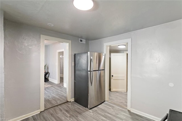 kitchen with light wood-type flooring, baseboards, visible vents, and freestanding refrigerator