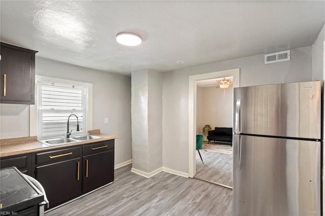 kitchen featuring light wood-style floors, freestanding refrigerator, visible vents, and a sink