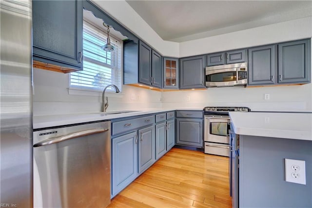 kitchen featuring glass insert cabinets, stainless steel appliances, light countertops, light wood-type flooring, and a sink