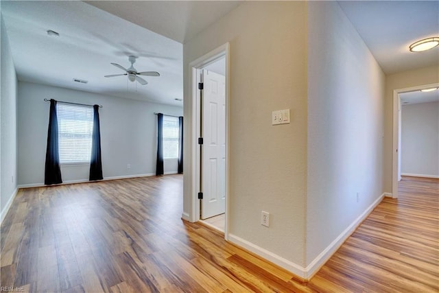 corridor with light wood-style flooring, visible vents, and baseboards