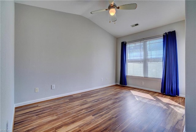 empty room with lofted ceiling, visible vents, a ceiling fan, wood finished floors, and baseboards