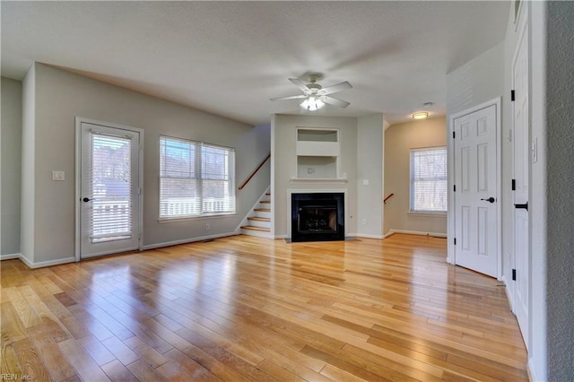 unfurnished living room featuring light wood finished floors, a fireplace, a ceiling fan, and baseboards