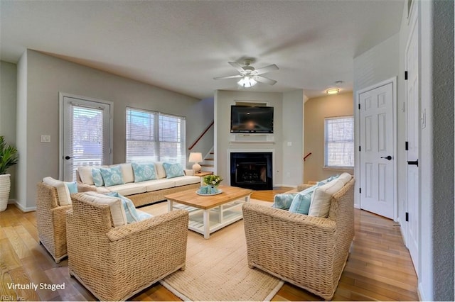 living room featuring ceiling fan, light wood finished floors, a fireplace, and baseboards