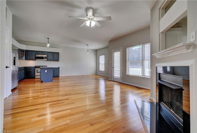 unfurnished living room featuring ceiling fan, a fireplace with flush hearth, baseboards, an AC wall unit, and light wood-type flooring