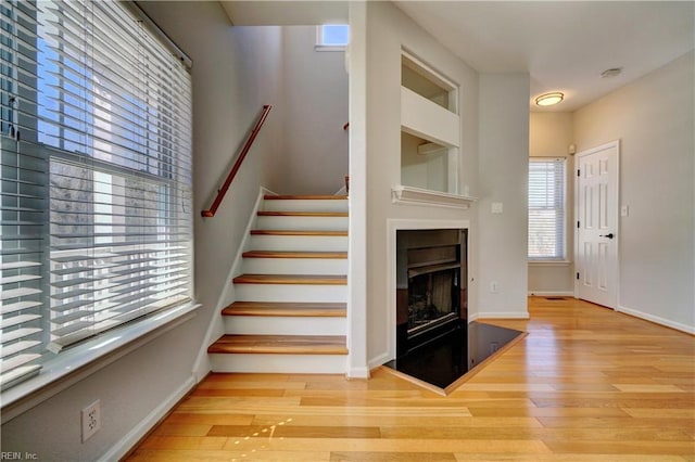 stairway featuring baseboards, a fireplace with raised hearth, and wood finished floors