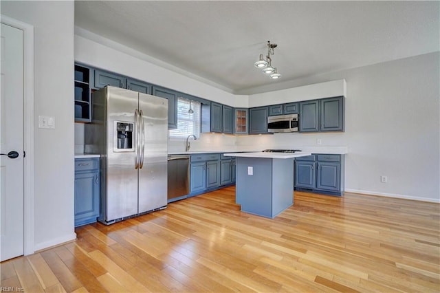 kitchen featuring a sink, light countertops, appliances with stainless steel finishes, open shelves, and light wood finished floors