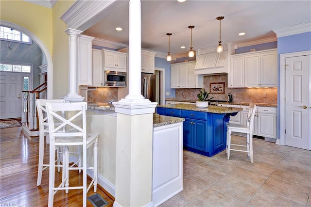 kitchen featuring premium range hood, appliances with stainless steel finishes, decorative columns, and blue cabinets