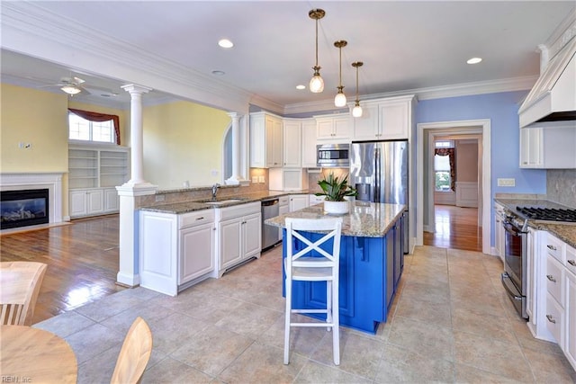 kitchen featuring a glass covered fireplace, stainless steel appliances, ornate columns, white cabinetry, and a sink