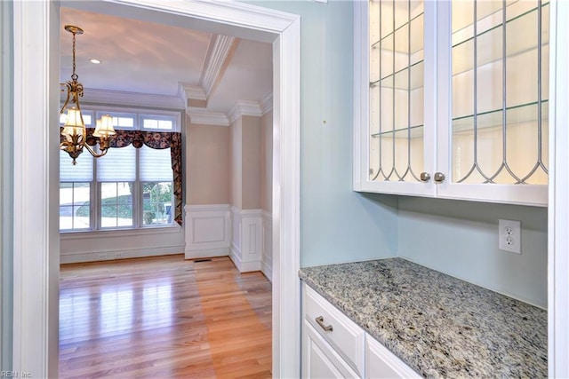 interior space featuring light stone counters, light wood-style flooring, ornamental molding, white cabinets, and a chandelier