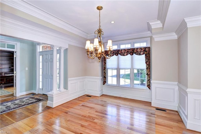 interior space with a wainscoted wall, ornamental molding, ornate columns, light wood finished floors, and an inviting chandelier