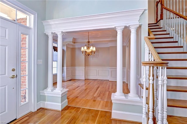 foyer featuring light wood-style floors, wainscoting, stairs, and ornate columns