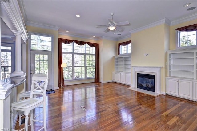 unfurnished living room featuring a healthy amount of sunlight, wood finished floors, and ornate columns