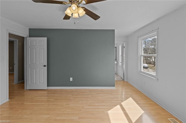 spare room with light wood-type flooring, visible vents, ceiling fan, and baseboards